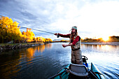 A fly fisher casting his line out of a boat while fly fishing surrounded by fall colors in Montana., Bozeman, Montana, USA