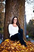 A beautiful young woman smiling while sitting under a large tree in the fall in Idaho., Sandpoint, Idaho, USA