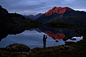 One man silhouetted against a lake after sunset drinking from a bottle., Anchorage, Alaska, USA