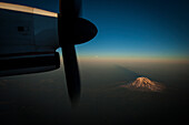 A snow capped mountain seen at sunset through an airplane window with the propeller as a frame., Anchorage, Alaska, USA