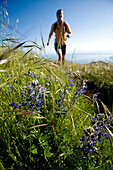 A woman hiking in grassy hills along the coast with a flower in the foreground San Francisco, California, USA