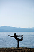 Silhouette of a woman doing yoga on a beach by a lake in the mountains South Lake Tahoe, California, USA