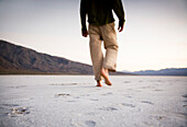 A man walks barefoot on the salt flats of Death Valley National Park, California Death Valley National Park, California, USA