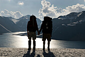 Two backpackers hold hands while overlooking a high alpine lake and distant mountains Chile