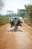 Peddler with water containers on a motorbike passing a road to Kabini, Karnataka, India