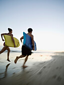 Multi-ethnic couple running with surfboards, Newport Beach, CA
