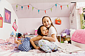 Asian sisters hugging on bed, Seattle, WA