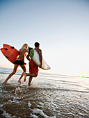 Couple running on beach carrying surfboards, Newport Beach, CA, USA
