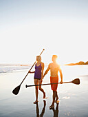 Couple walking on beach carrying paddles, Newport Beach, CA, USA