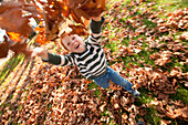 Caucasian boy throwing autumn leaves, Nanaimo, British Columbia, Canada