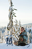 Caucasian woman snowshoeing in remote area taking break, North Vancouver, British Columbia, Canada