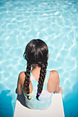 Hispanic girl sitting on diving board over swimming pool, Huntington Station, New York, USA