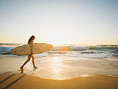 Gemischtrassige Frau mit Surfbrett am Strand, Laguna Beach, Kalifornien, USA