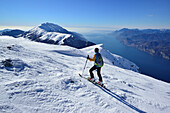 Female back-country skier ascending to Monte Baldo, lake Garda in background, Monte Baldo, Garda mountains, Trentino, Italy