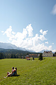 Paar sitzt auf einer Wiese, Schloss Kranzbach im Hintergrund, Klais, Krün, Oberbayern, Bayern, Deutschland