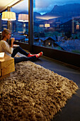 Woman sitting on floor in a hotel winter garden while enjoying view in the evening, Adelboden, Canton of Bern, Switzerland
