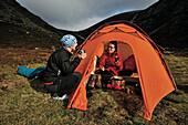 Hikers having breakfast at a tent, Creag an Dubh Loch, Cairngorms, Grampian Mountains, Highlands, Scotland, Great Britain