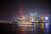Sightseeing boat on the Huangpu River with Oriental Pearl Tower and Pudong skyline at night, Shanghai, China