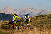 Mountain bikers passing Winklmoosalm, Berchtesgaden Alps in background, Chiemgau, Upper Bavaria, Germany
