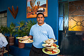 Waiter serving plates with Mexican food in a hotel restaurant, Todos Santos, Baja California Sur, Mexico