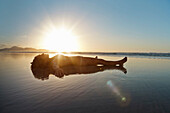 Mid adult woman lying in shallow water on beach at sunset