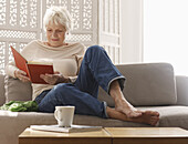 Senior woman relaxing on sofa with book