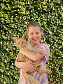 Young girl holding pet cat, smiling, portrait