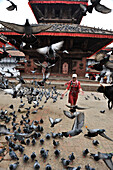 Woman running through a flock of pigeons in front of Jagannath Temple in Durbar Square of Kathmandu, Nepal