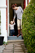 Mother helping toddler son over front doorstep