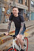 Young tattooed man cycling on street, smiling