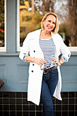 Mature woman in white coat and jeans, smiling
