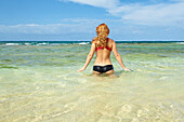 'A young woman in a bikini enters the ocean water; Wailua, Hawaii, United States of America'