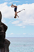 'A young man enjoys a 30 foot high jump at ''da big rock'' in Waimea Bay; North Shore, Oahu, Hawaii, United States of America'