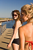 Two Young Women Walking Along Pier, Rear View