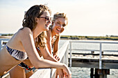 Two Young Women Leaning on Railing on Side of Pier