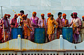 Men stands on top of the temple throwing colors over the people on the ground floor in Nandgaon, Mathura, India