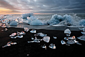 At sunset the mighty ocean waves crush onto the little icebergs on the black sand beach at Jokulsarlon, Iceland