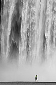 A young woman stands in front of the giant wall of water of the Skogafoss waterfall, Iceland