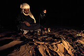 Berber man with turban serves tea in the desert at night on a carpet over the sand, Sahara desert, Morocco