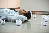 Businessman on floor surrounded by crumpled paper, Cape Town, Western Cape, South Africa