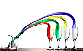 four glasses pour their colored liquid in a fifth glass.