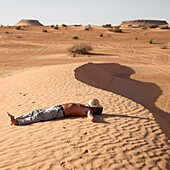 Man lying on sand in the Sahara. Tunisia.