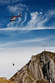 'Helicopter Rescue On A Mountain Side With A Cross On The Top Of The Mountain; Fussen, Germany'