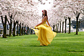 Woman In Yellow Dress Dancing Among Flowering Trees