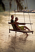 'Couple Sits On Beach Swing At Sunset; Koh Tao, Thailand'