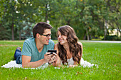 'Young Couple Looking At Text Messages Together In The Park; Edmonton, Alberta, Canada'