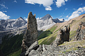 'Large Rock Sentinels On Mountain Ridge With A Mountain Range And Valley In The Background With Blue Sky And Clouds; Alberta, Canada'