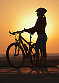 'A Cyclist Stands On The Beach With Her Bike At Sunset; Tarifa, Cadiz, Andalusia, Spain'