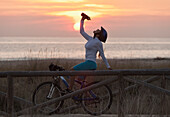 'A Cyclist Stops For A Drink On A Wooden Boardwalk Along The Ocean; Tarifa, Cadiz, Andalusia, Spain'