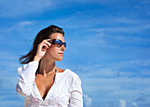 'Portrait Of A Woman Wearing Sunglasses Against A Blue Sky; Punta Cana, La Altagracia, Dominican Republic'